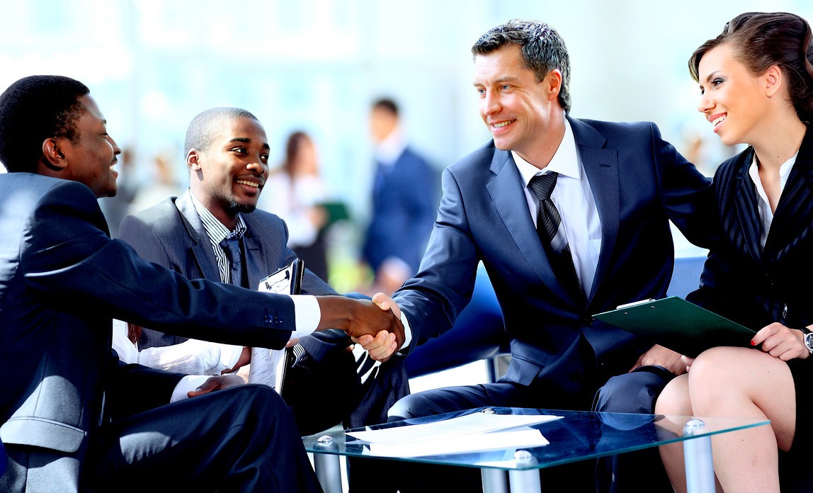 Two men in suits shaking hands at a table.